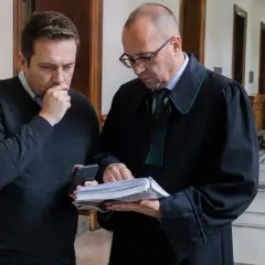 Mężczyzna w szacie prawniczej pokazuje dokumenty drugiemu mężczyźnie, który wygląda na zmartwionego. Sprawa dotyczy gwałtu na mężczyźnie.
