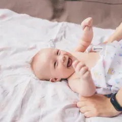 Radość maluszka, kiedy dziecko zaczyna się uśmiechać. Ręce rodzica delikatnie trzymają jego nóżki.