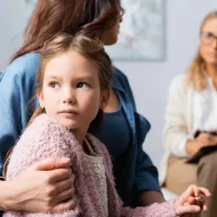 Dziewczynka przytulona do mamy, zamyślona. Terapia pomaga jej radzić sobie z syndromem braku ojca u córki.