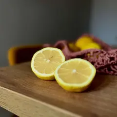 Dwa połówki cytryny na drewnianym blacie, obok różowej siatki z cytrynami. To proste rzeczy, jakie wpływają dobrze na samopoczucie.