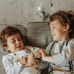 Dwóch chłopców na kanapie, jeden łapie drugiego za rękę. Może to być początek zabawy lub przejaw agresji wobec młodszego rodzeństwa.