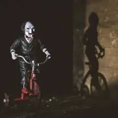 Lalka Billy z Piły na czerwonym trójkołowcu, jej cień na ścianie przypomina o najlepszych horrorach psychologicznych.