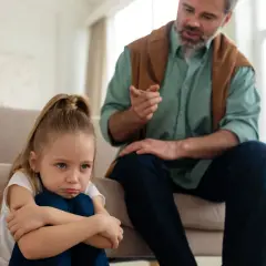 Smutna dziewczynka siedzi na podłodze, podczas gdy ojciec mówi do niej ostro, ukazując typowe daddy issues zachowania.