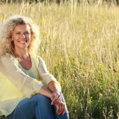 Uśmiechnięta kobieta po 50. siedzi na łące pełnej traw i kwiatów. Jestem samotna po 50. i cieszę się chwilą spokoju.