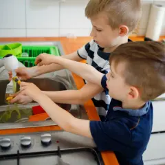 Dwóch chłopców myje pędzle pod bieżącą wodą. To ich obowiązki dziecka w domu, uczą się odpowiedzialności.