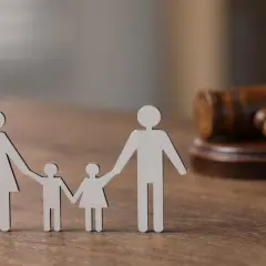 Drewniane figurki rodziny i młotek sędziowski symbolizują sprawiedliwość i potencjalną karę za manipulowanie dzieckiem w sprawach rodzinnych.