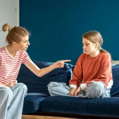 Matka z wyrzutem wskazuje palcem na córkę, która siedzi z opuszczoną głową. Scena sugeruje odrzucenie matki przez dorosłe dziecko.