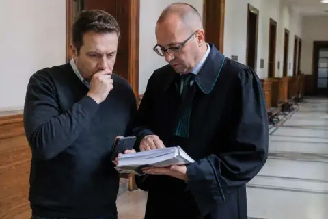 Mężczyzna w szacie prawniczej pokazuje dokumenty drugiemu mężczyźnie, który wygląda na zmartwionego. Sprawa dotyczy gwałtu na mężczyźnie.