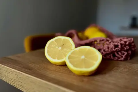 Dwa połówki cytryny na drewnianym blacie, obok różowej siatki z cytrynami. To proste rzeczy, jakie wpływają dobrze na samopoczucie.