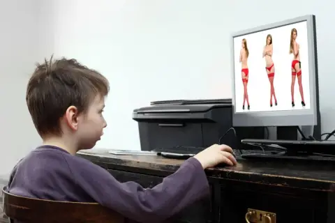 Chłopiec patrzy na ekran komputera, na którym wyświetlone są zdjęcia kobiet w bieliźnie.