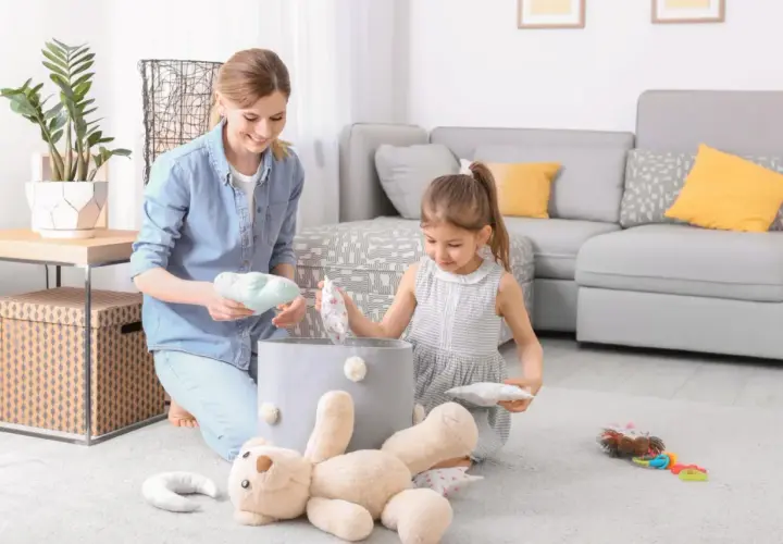 Mama i córka sprzątają zabawki. Dziecko uczy się obowiązków w domu, jakby obowiązywała ustawa o porządku.