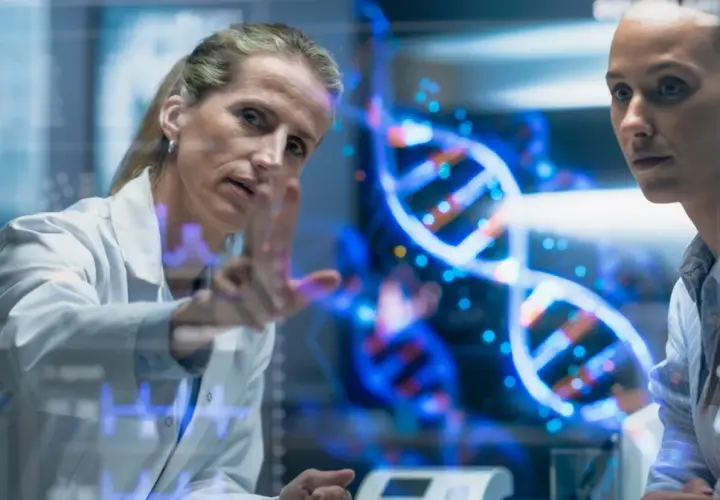Naukowczyni analizuje na ekranie spiralę DNA, dyskutując z koleżanką, czy to geny czy wychowanie kształtują człowieka.