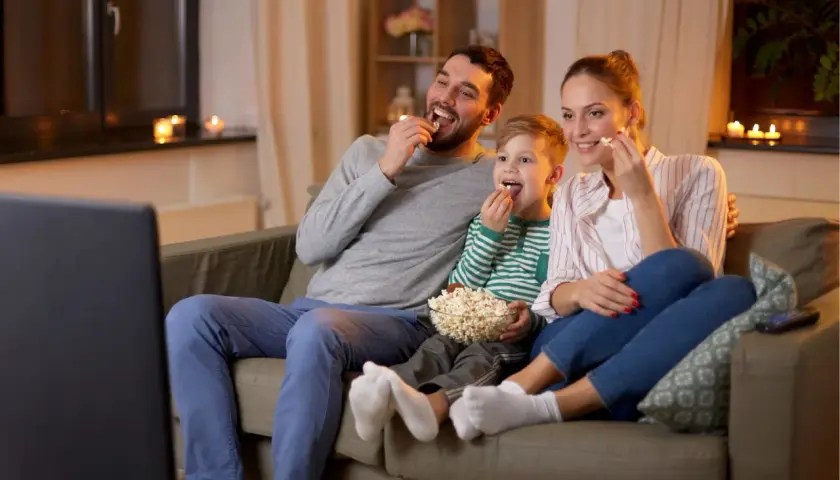 Rodzina ogląda filmy o rodzinie, zajadając popcorn. Radość i wspólne chwile na kanapie.