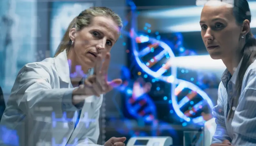 Naukowczyni analizuje na ekranie spiralę DNA, dyskutując z koleżanką, czy to geny czy wychowanie kształtują człowieka.