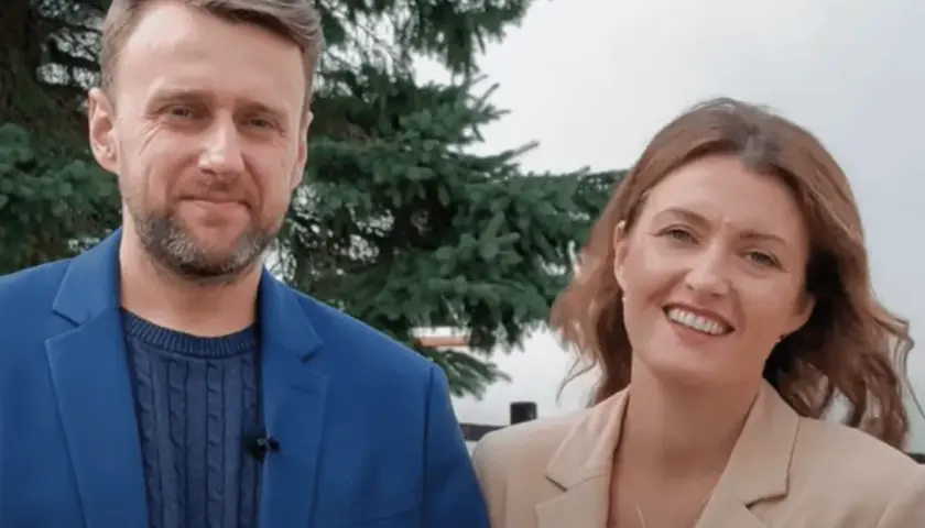 Uśmiechnięta para, on w niebieskiej marynarce, ona w beżowej. Wyglądają jak towarzystwo wzajemnej adoracji, ciesząc się wspólnym momentem.