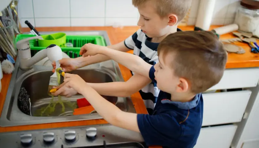 Dwóch chłopców myje pędzle pod bieżącą wodą. To ich obowiązki dziecka w domu, uczą się odpowiedzialności.