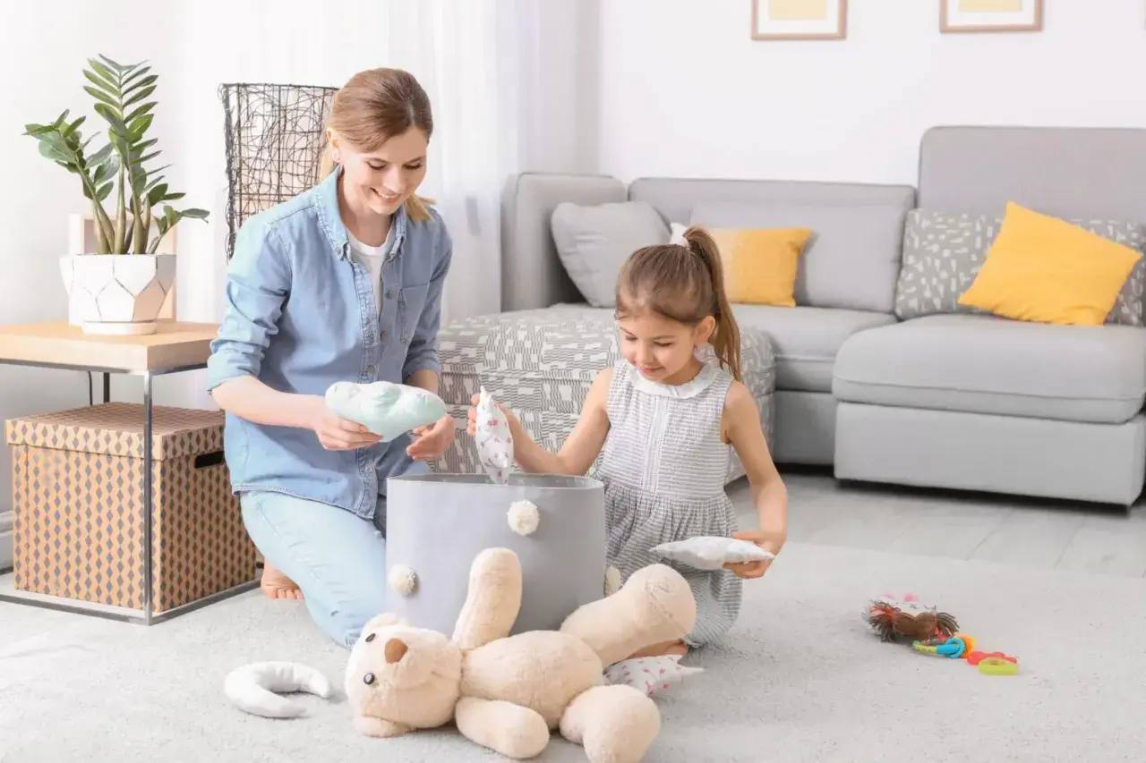 Mama i córka sprzątają zabawki. Dziecko uczy się obowiązków w domu, jakby obowiązywała ustawa o porządku.