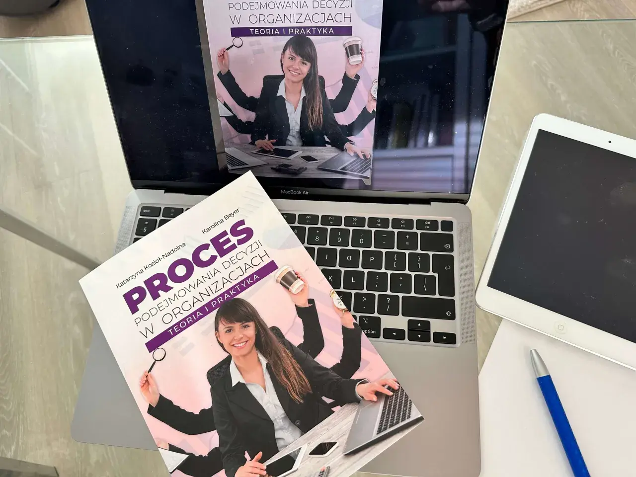Książka "Proces podejmowania decyzji w organizacjach" na laptopie. Ilustracja sugeruje teorię racjonalnego wyboru, gdzie wieloręka kobieta zarządza wieloma zadaniami.