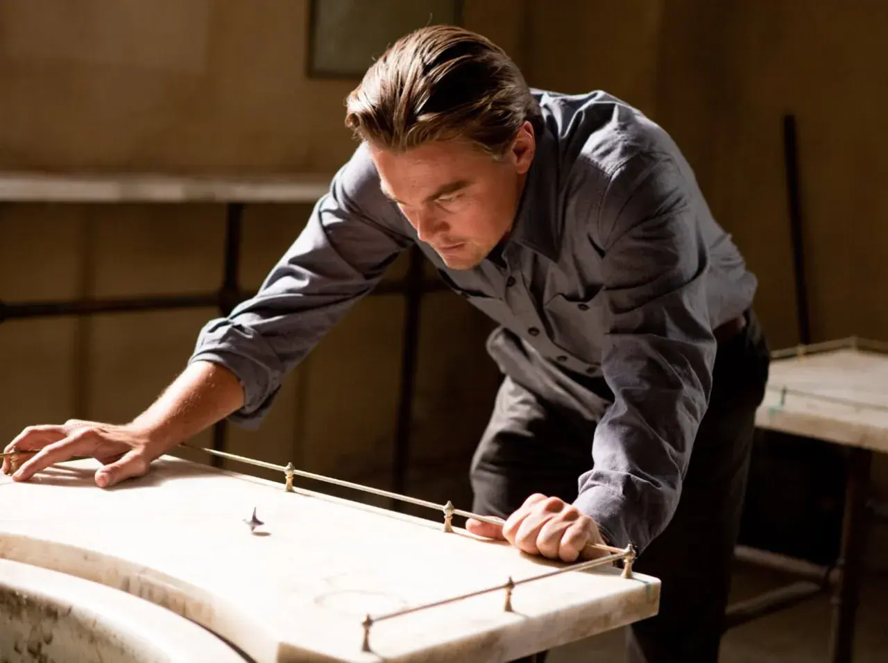 Leonardo DiCaprio pochyla się nad stołem, obserwując wirujący bączek. Czy to jego sposób na zrozumienie, czym jest incepcja?