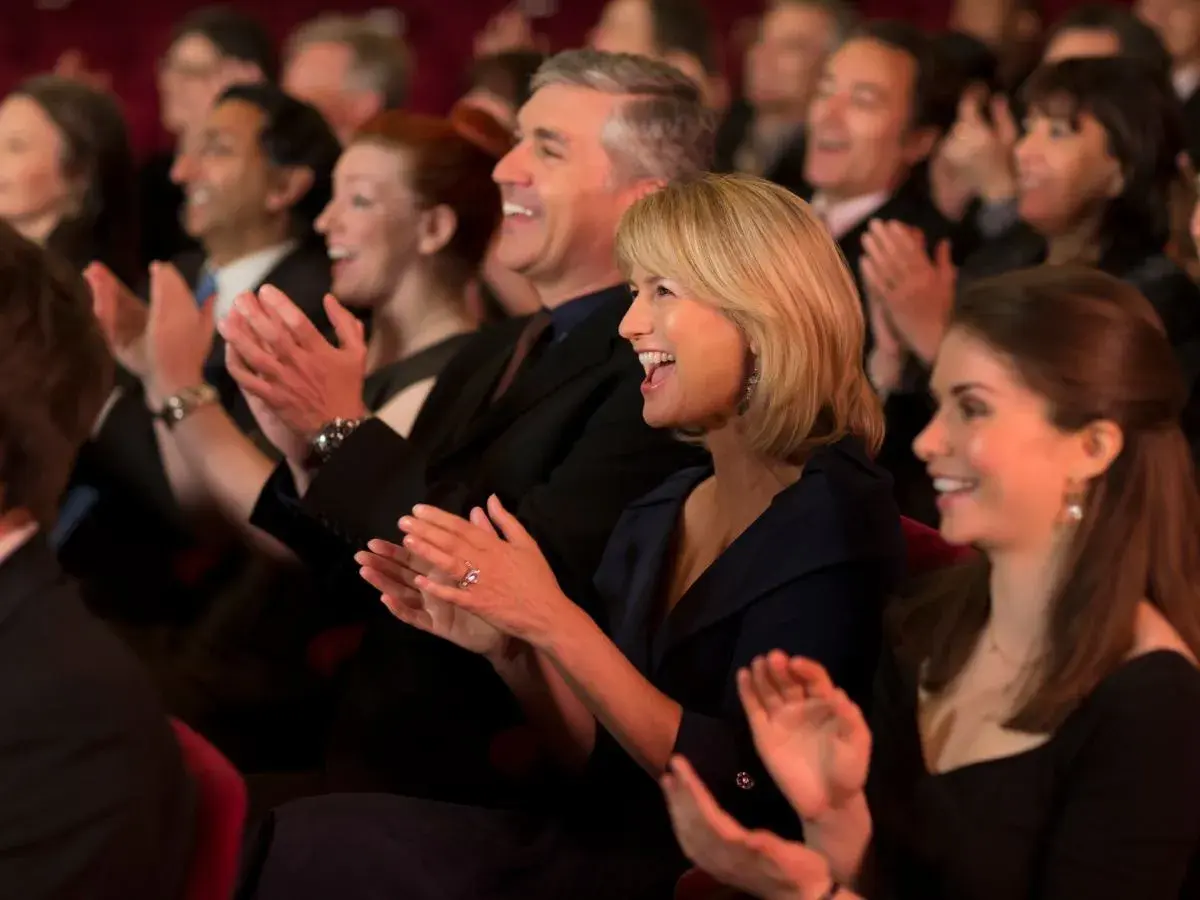 Ludzie klaszczą na widowni teatru. Elegancko ubrani, pokazują, jak się ubrać do teatru.