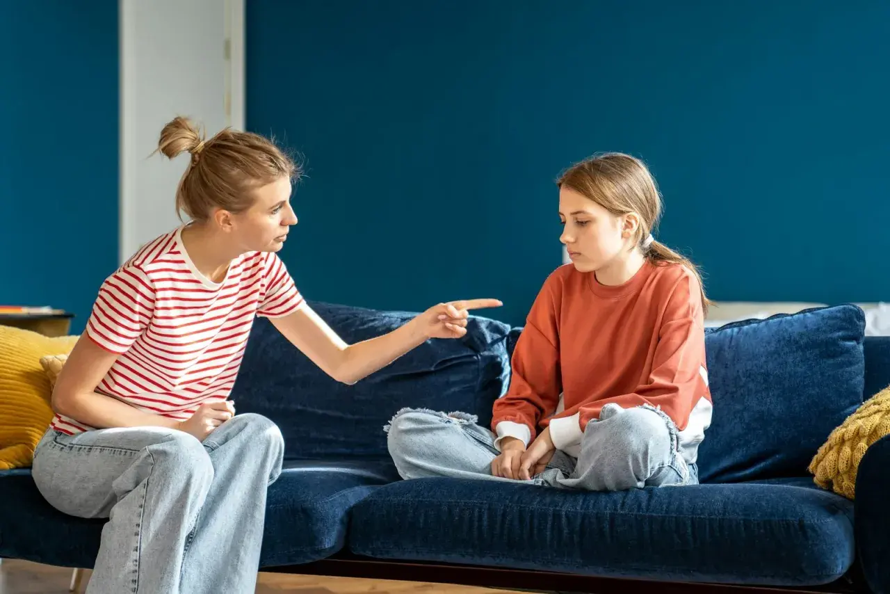 Matka z wyrzutem wskazuje palcem na córkę, która siedzi z opuszczoną głową. Scena sugeruje odrzucenie matki przez dorosłe dziecko.
