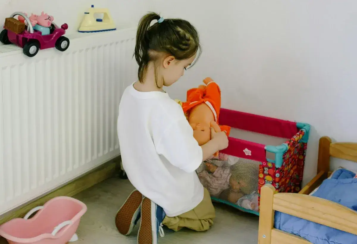 Dziecko bawi się lalką, udając, że opiekuje się nią jak niemowlęciem.