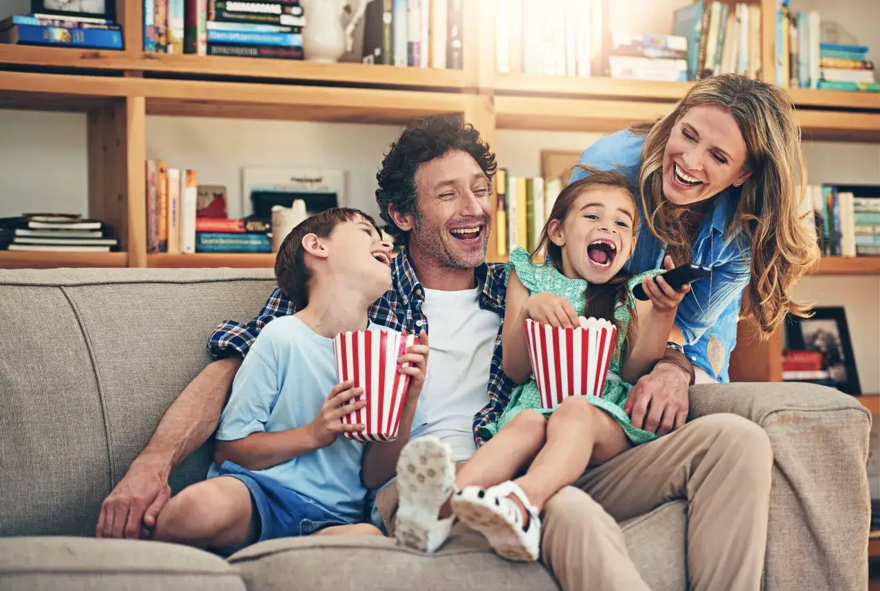 Rodzina śmieje się podczas oglądania filmów o rodzinie, jedząc popcorn.