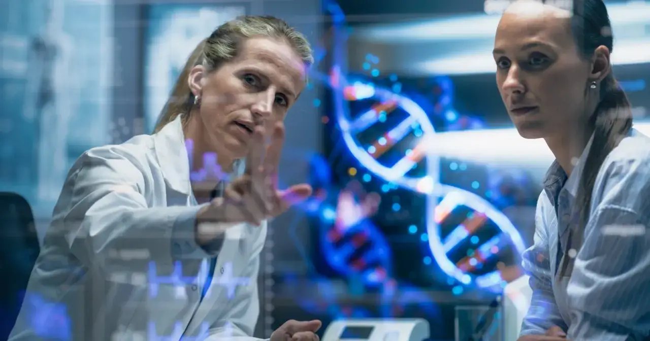 Naukowczyni analizuje na ekranie spiralę DNA, dyskutując z koleżanką, czy to geny czy wychowanie kształtują człowieka.