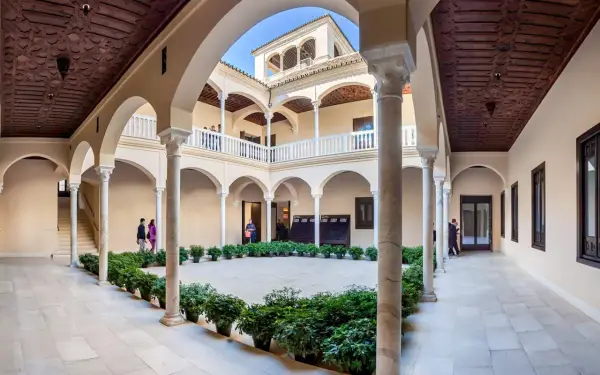 Wnętrze muzeum Picassa w Maladze, z dziedzińcem otoczonym arkadami, zdobionymi drewnianymi stropami i rzędami zieleni.